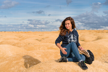 Beautiful young woman in a sweatshirt with an inscription sits on the sand in the desert with sand dunes of bizarre shape