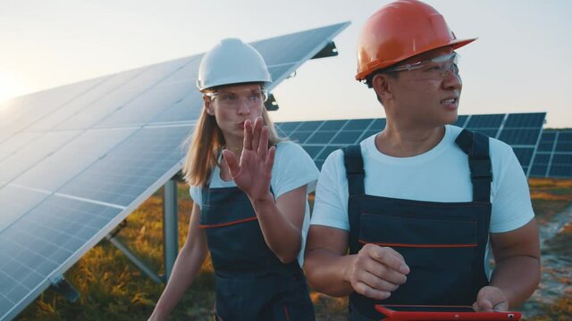 Female and male power engineers with tablet computer discuss installation of photovoltaic electricity in large eco-friendly industrial solar power plant. Clean energy concept.