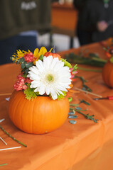Vertical photo of the thanksgiving autumn bouquet in a pumpkin on the table with the orange table cloth