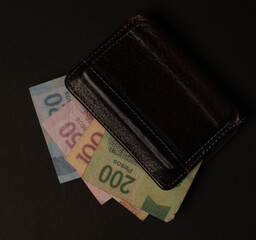 billetes de 200 100 50 y 20 pesos asomandose de una cartera cafe sobre fondo negro