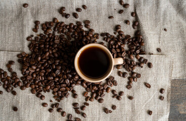 Coffee cup with roasted coffee beans on linen background. Mug of black coffe with scattered coffee beans. Fresh coffee beans.