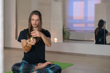 A young male yogi meditates and sings a mantra and prays while holding a bell in the Studio in the...