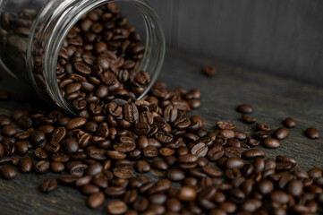 Roasted fresh arabica coffee beans scattered on a table from a little jar on a wooden table. Fresh coffee beans.
