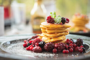 Delicious homemade pancakes with summer berries fruit for breakfast. Morning meal pancakes topped with honey on black dish.