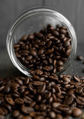 Roasted fresh arabica coffee beans scattered on a table from a little jar on a wooden table. Fresh coffee beans.
