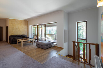 Modern interior of hall in luxury private house. Chess on table. Wooden chair. Leather couch. Glass door to terrace. Stairs down.