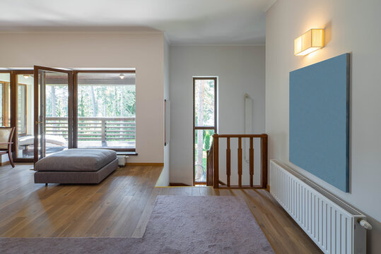 Light contemporary interior of private house. Cozy soft sofa. Glass door to terrace. Wooden staircase down.