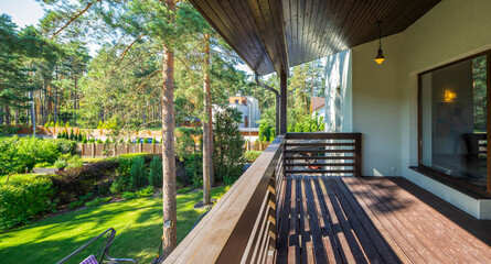 Modern wooden terrace in luxury cottage. Panorama window. Green garden with trees.