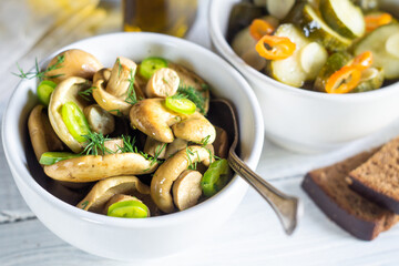 Salted milk mushrooms and pickled cucumbers in bowls on a white wooden table