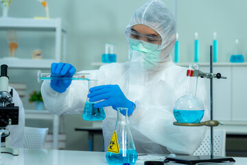 Fototapeta premium Asian medical scientist in protective white jumpsuit and glasses and face mask diagnosis virus with microscope in clinical laboratory