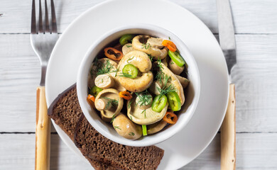 Pickled white mushrooms with peppers and herbs in a bowl on a white wooden table