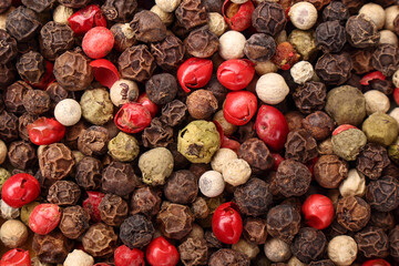 Top view of pile of various peppercorns, close up. Mix of black, white, green and red dried peppercorns.