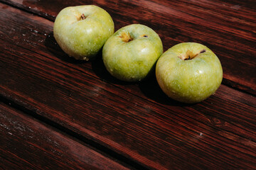 Fresh autumn Apple harvest on the kitchen countertop. Three fresh green apples lie in a row on a wooden table. A textured mahogany wood background and fruit lie on it.