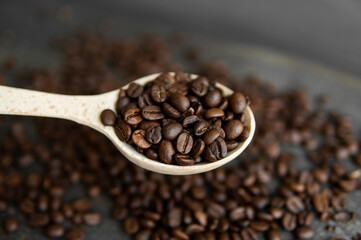 Fresh roasted arabica coffee beans in a wooden spoon and scattered coffee beans on a wooden table.