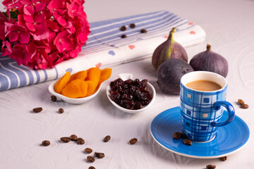 a cup of coffee, dried apricots and cranberries, fresh figs, a hydrangea branch and sprinkled coffee beans