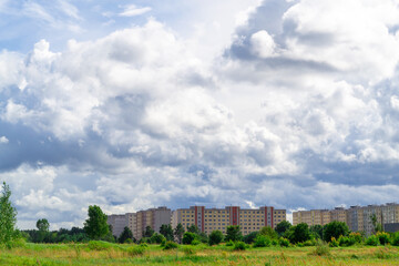Fototapeta na wymiar Dreilini microdistrict, Riga, Latvia. Nine storey buildings built in the 90s. And a green pone in the foreground. Gray cumulus dramatic clouds.