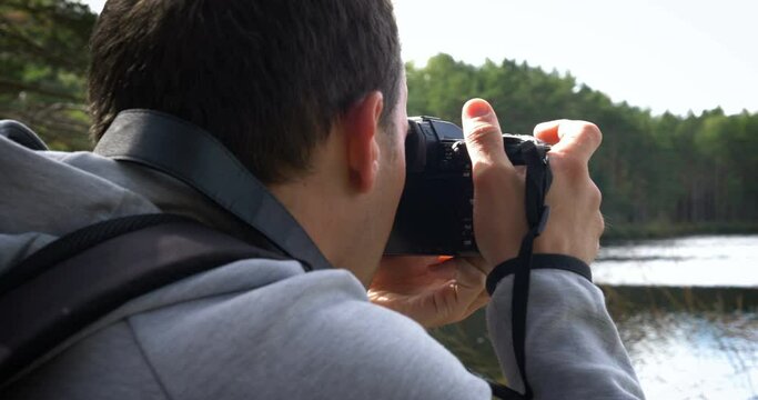 Photographer with professional photo camera and backpack on the top takes pictures of nature.