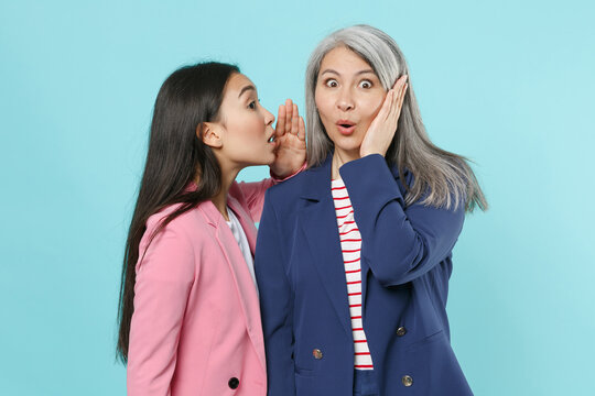 Shocked asian female business women employer employee in pink blue jackets work in office whispers gossip tells secret with hand gesture put hand on cheek isolated on blue background studio portrait.