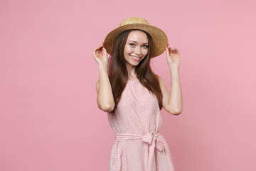 Smiling charming beautiful attractive young brunette woman 20s wearing pastel pink summer dotted dress hat posing standing and looking camera isolated on pastel pink background, studio portrait.