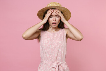 Frustrated sick tired young brunette woman 20s in pink summer dotted dress hat posing put hand on head having headache keeping eyes closed isolated on pastel pink color background studio portrait. © ViDi Studio