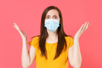 Shocked young woman in yellow t-shirt sterile face mask to safe from coronavirus virus covid-19 2019-ncov during pandemic quarantine spreading hands isolated on pink color background studio portrait.