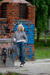 Beautiful blond women wearing casual striped hoodie outdoors, standing near graffiti-painted brick wall