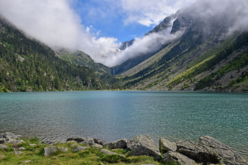 Green and cloudy mountain landscape with a large lake of transparent water, trees and clouds.