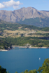 Fototapeta premium view of Serre Ponçon lake, France in the mountains with a lone sailboat
