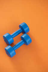 a pair of blue dumbbells on orange background. copy space.
