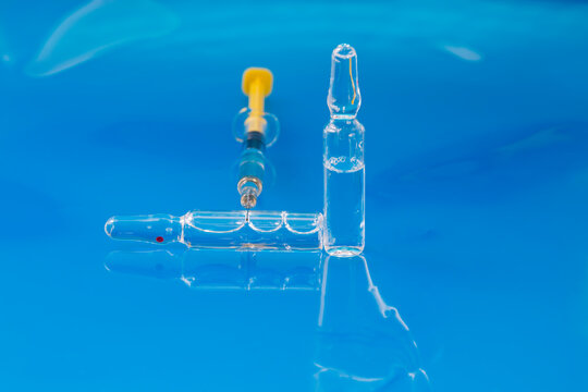 Glass ampoules containing injectable pharmaceuticals and syringe for intramuscular or intravenous injection on blue background