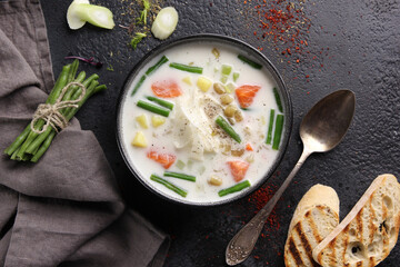 Creamy soup with salmon, asparagus beans, potatoes and croutons in a deep bowl on a black background. Flatlay, horizontal. Background image, copy space
