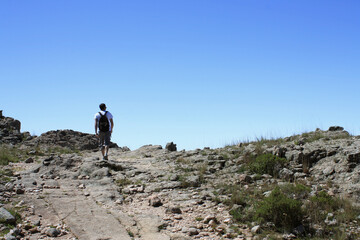 Fototapeta premium Outdoor activities. Hiking. View of a young adult hiker, walking along the dirt path in the rocky mountain top. 