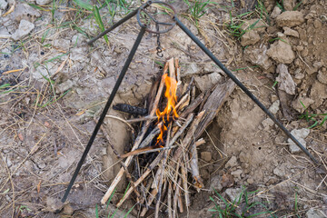 Lighting a fire on a picnic. The firewood is burned in a specially dug pit to avoid fire. Tripod for the cauldron is stand above the pit