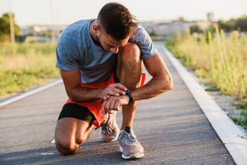 Young handsome sporty jogger taking break from exercising outdoors looking on a smart fitness watch