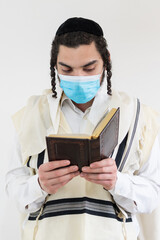 Orthodox Jewish man praying with prayer shawl, tallit, over his head, wearing protective mask...