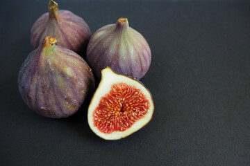 half a ripe juicy Fig and three whole purple ones with green figs on the back on a black background side view. fruit antioxidants