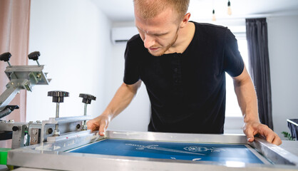 Selective focus of artisan holding frame with stencils of screen printing press in workshop 