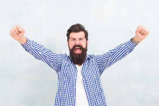Happy bearded man celebrate victory keeping arms upward fingers clenched winning gestue blue background, winner