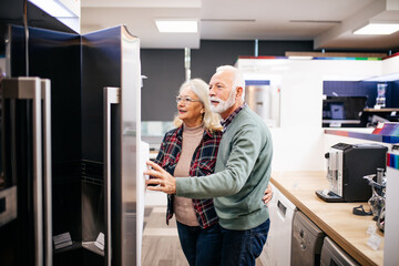 Senior husband and wife, satisfied customers choosing fridges in appliances store.