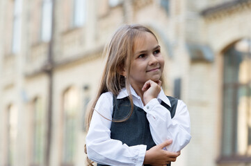 Happy little child lost in thoughts with thoughtful look in school uniform outdoors, thinking