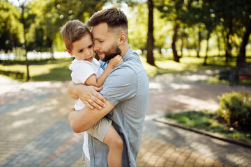 Handsome man with little boy at the park, lovely son sitting on fathers arms, smiling, dad and toddler spend time together, enjoy tender family moments, parenthood concept