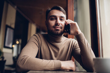 Positive young guy talking on smartphone in coffee house