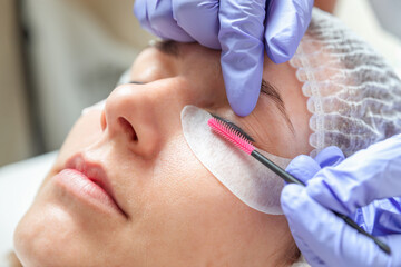 Young woman makes eyelash lamination procedure in a beauty salon, close-up.