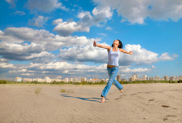 Fototapeta premium Joyful young woman in blue jeans jumping on sandy beach outside city