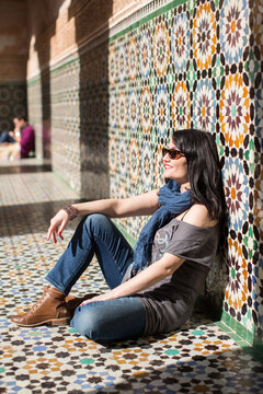 Side view of woman sitting against tiled wall, Ben Youssef Madras, Marrakesh, Morocco