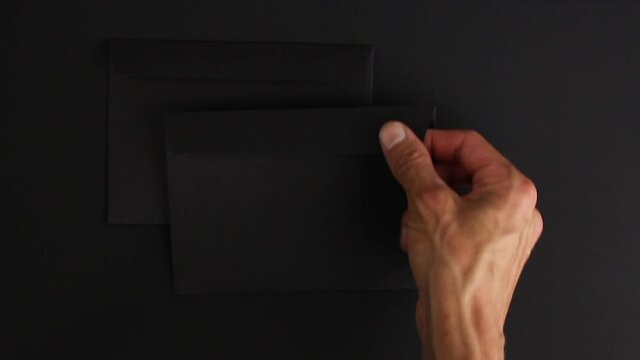 caucasian male hand take three strange blank black envelopes from black background, mysterious message, mockup with empty space, dark mood