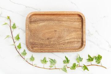 Flat lay of wooden tray and Green ivy leaves on white marble background. Mock up