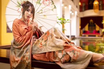 Young woman wearing a kimono, Japanese culture with an umbrella,  looking at the camera. Japanese concept of kimono and yukata.