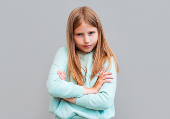 Frustrated upset lonely little girl standing in closed pose isolated on gray studio background, lonely offended blonde kid weeping feel unhappy, anxiety disorder or naughty bad behavior concept