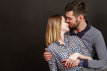 Beautiful couple kissing while sitting against of black background. Studio shot